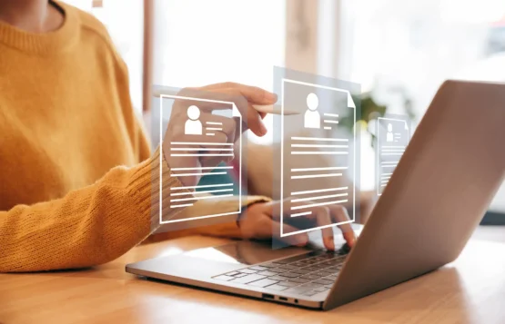 Imagem de uma pessoa usando um notebook com alguns elementos gráficos de currículos aparecendo em frente a tela