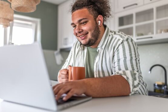 Imagem de um homem com uma xícara olhando o computador na bancada de sua casa