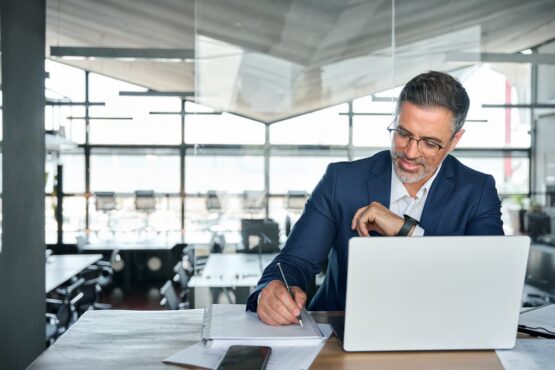 Imagem de um homem no escritório escrevendo no papel na frente do computador