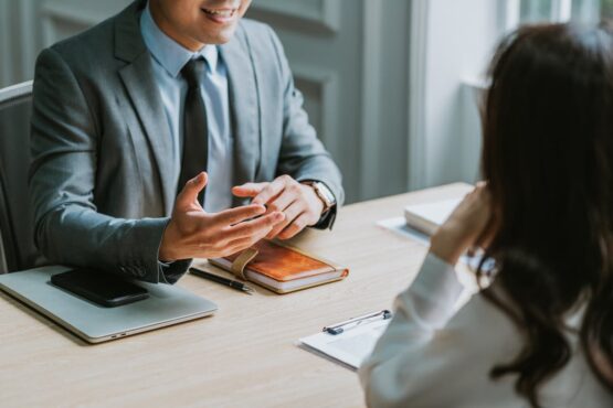 Imagem de um homem entrevistando uma mulher sentados na mesa de madeira