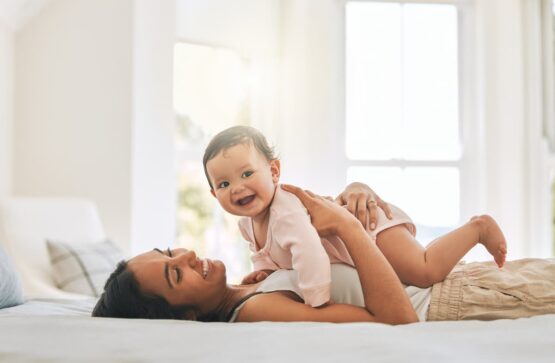 Imagem de uma mãe deitada na cama com o seu bebê em cima dela