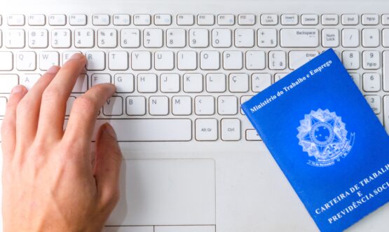 Mãos de uma pessoa sob um notebook e uma carteira de trabalho física.