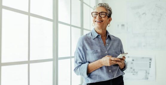 Imagem de uma mulher sorridente com o celular na mão no escritório