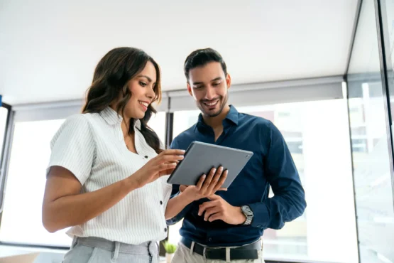 Imagem de um homem e uma mulher olhando para um tablet em um ambiente de trabalho