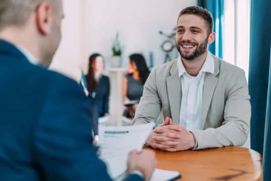 Imagem de um homem sorridente de terno claro, parece estar participando de uma entrevista