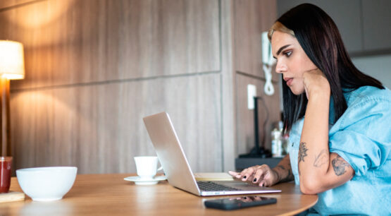 pessoa trans mexendo no computador, com expressão pensativa